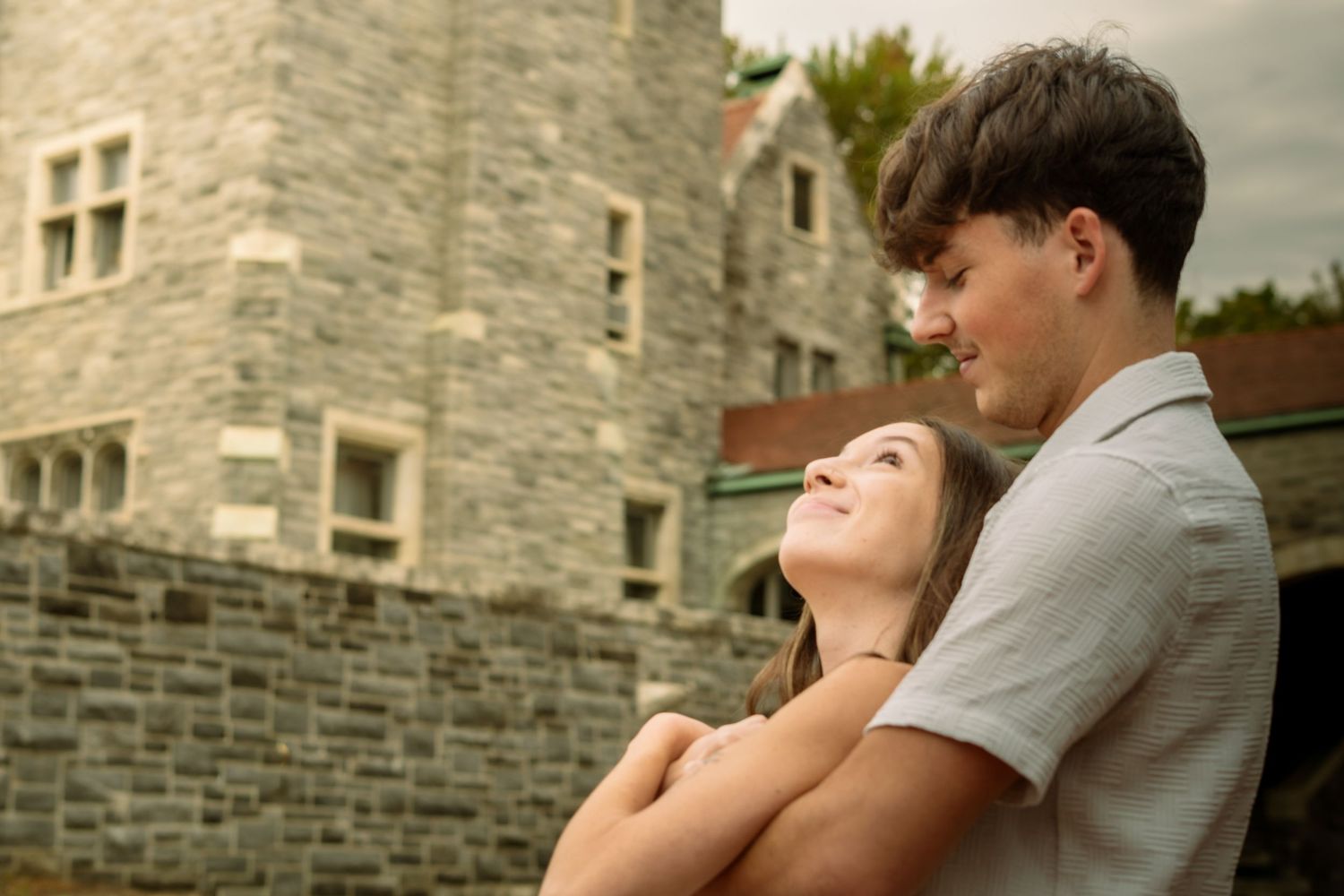 A couple shares an intimate moment together while leaning against a stone building wall.