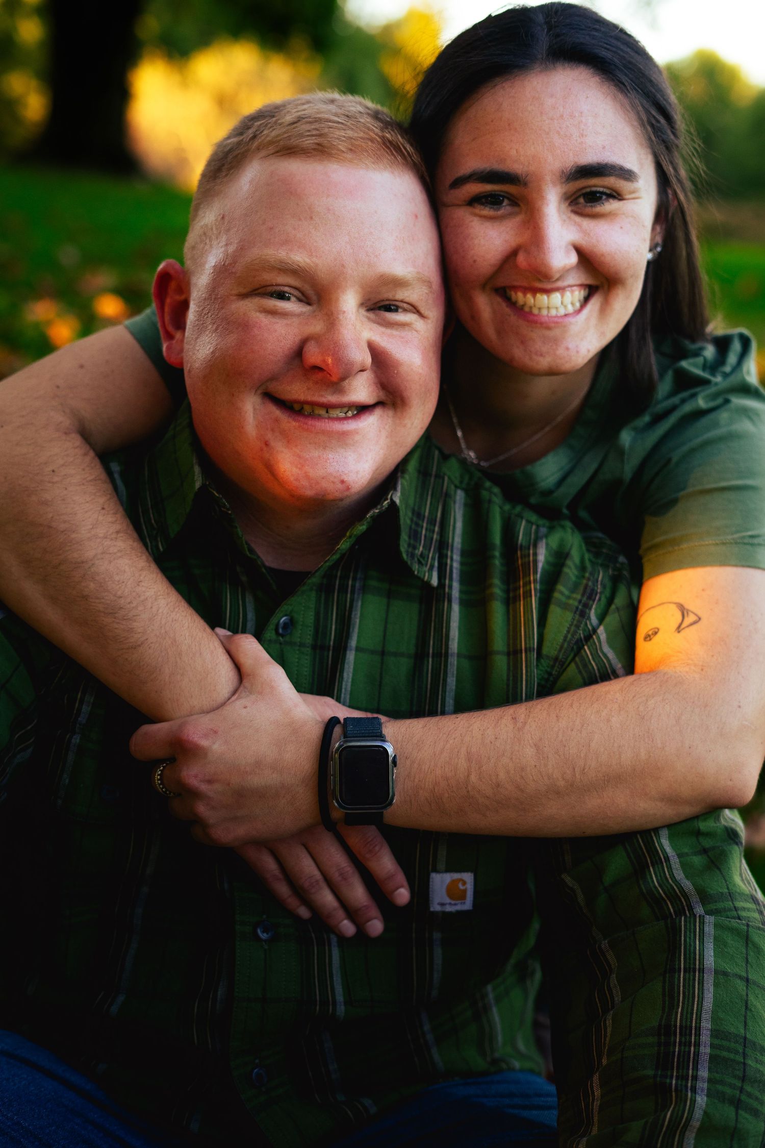 a young couple smiling at the camera. the girl putting her arms around and embracing her boyfriend in their matching green outfits. fall