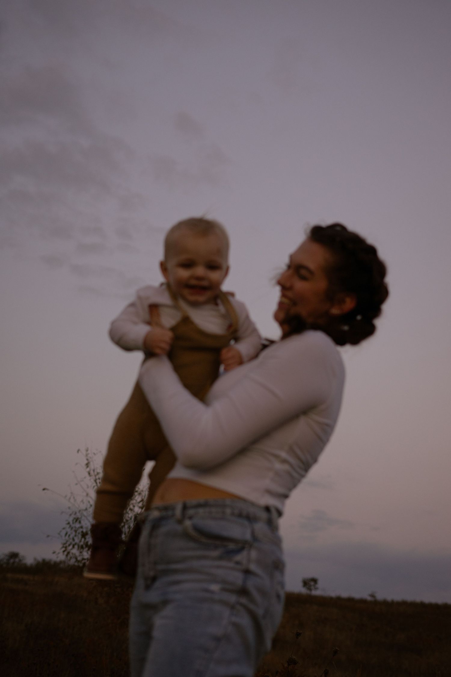 a mother smiling while lifting her son up. her son laughing from being picked up. the sky is purple hued in the grainy image