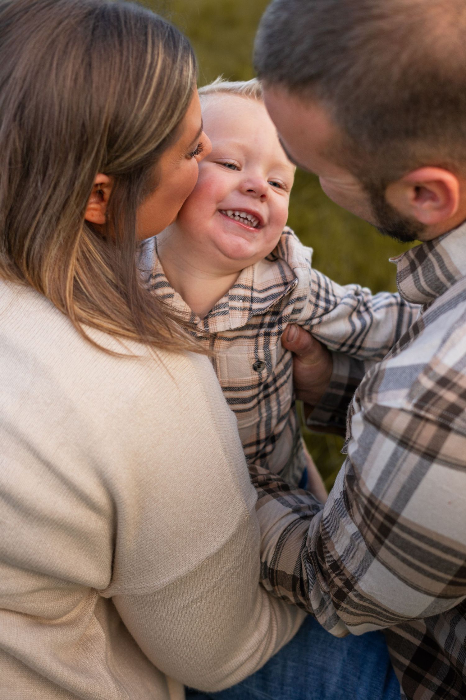 a man and woman crouching down to the son, embracing while his mom kisses his cheek. the man and the son are wearing matching flannel shirts