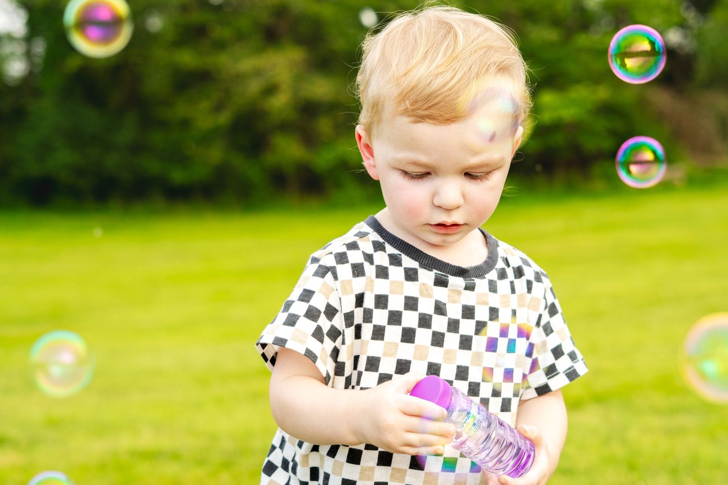 Child in black and white polka dot dress playing with bubbles in a sunny green garden.