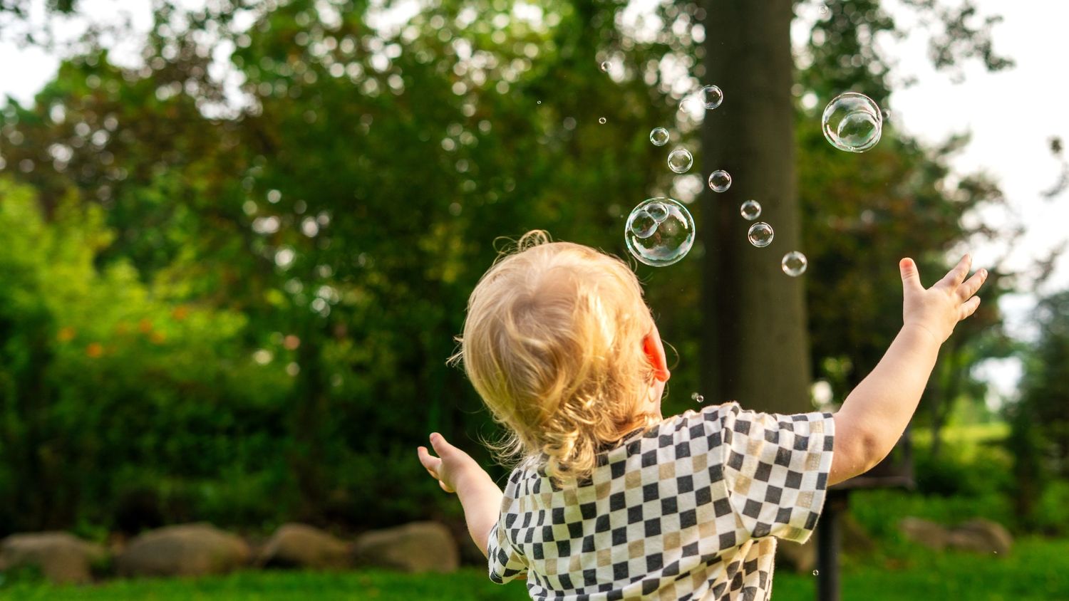 Delightful bubbles float through a lush backyard garden setting while a child plays on a summer afternoon.