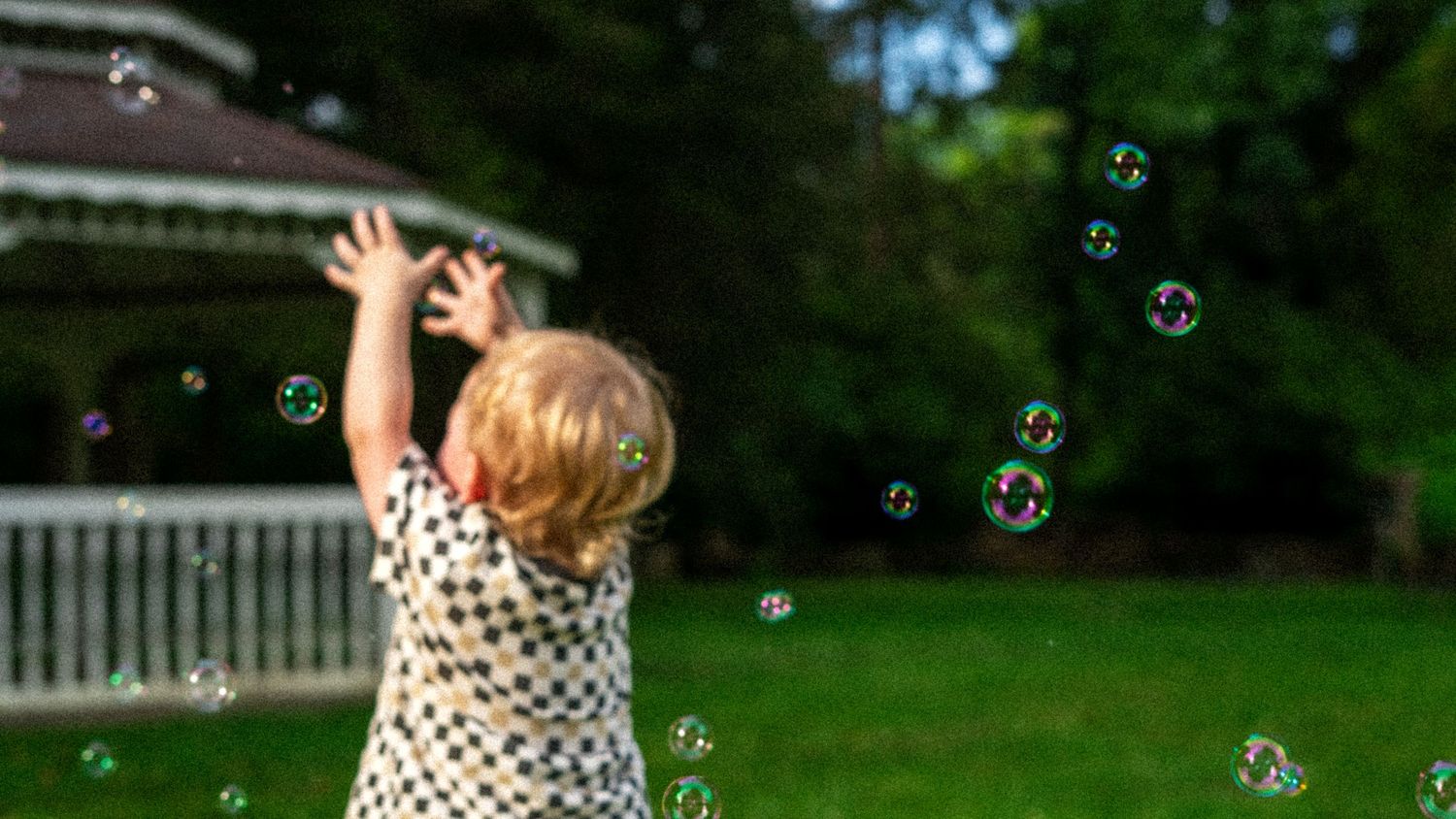 Happy young children chase soap bubbles floating in a sunny summer garden setting.