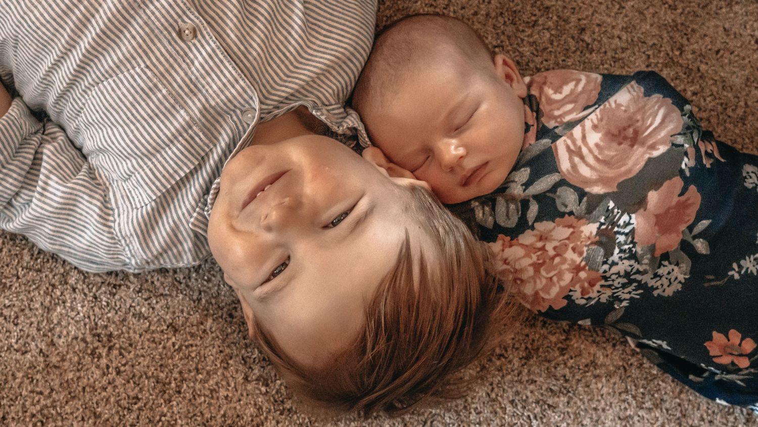 Two people touching foreheads while lying on a brown woven blanket in an intimate pose.