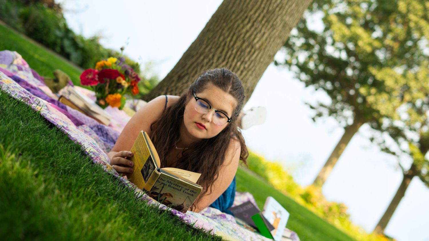 Person in vintage-inspired brown dress laying on grass during outdoor photoshoot in natural setting.