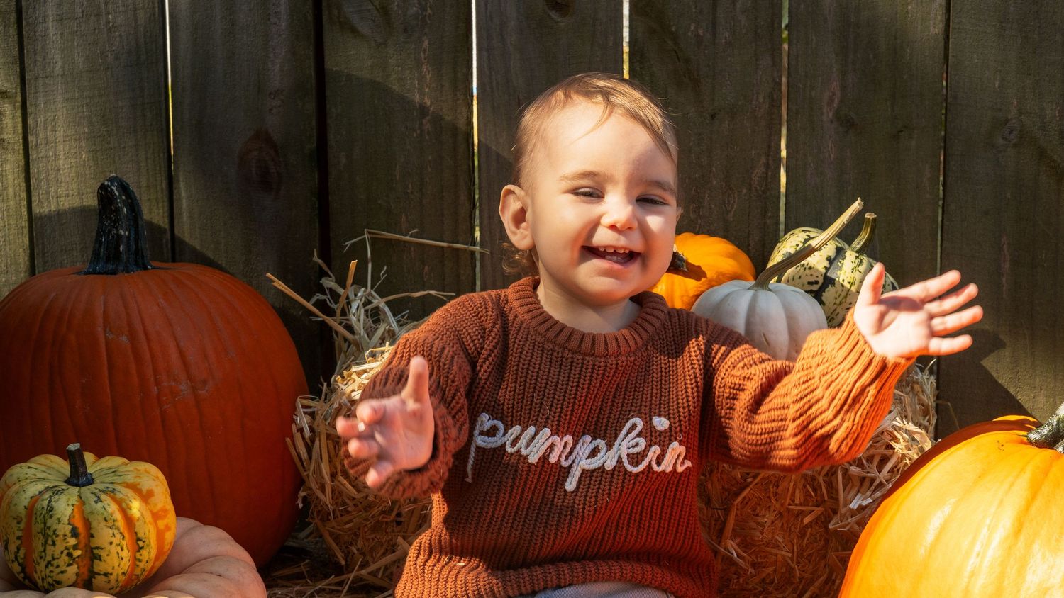 Three young children pose with pumpkins and fall decorations at an autumn harvest display.