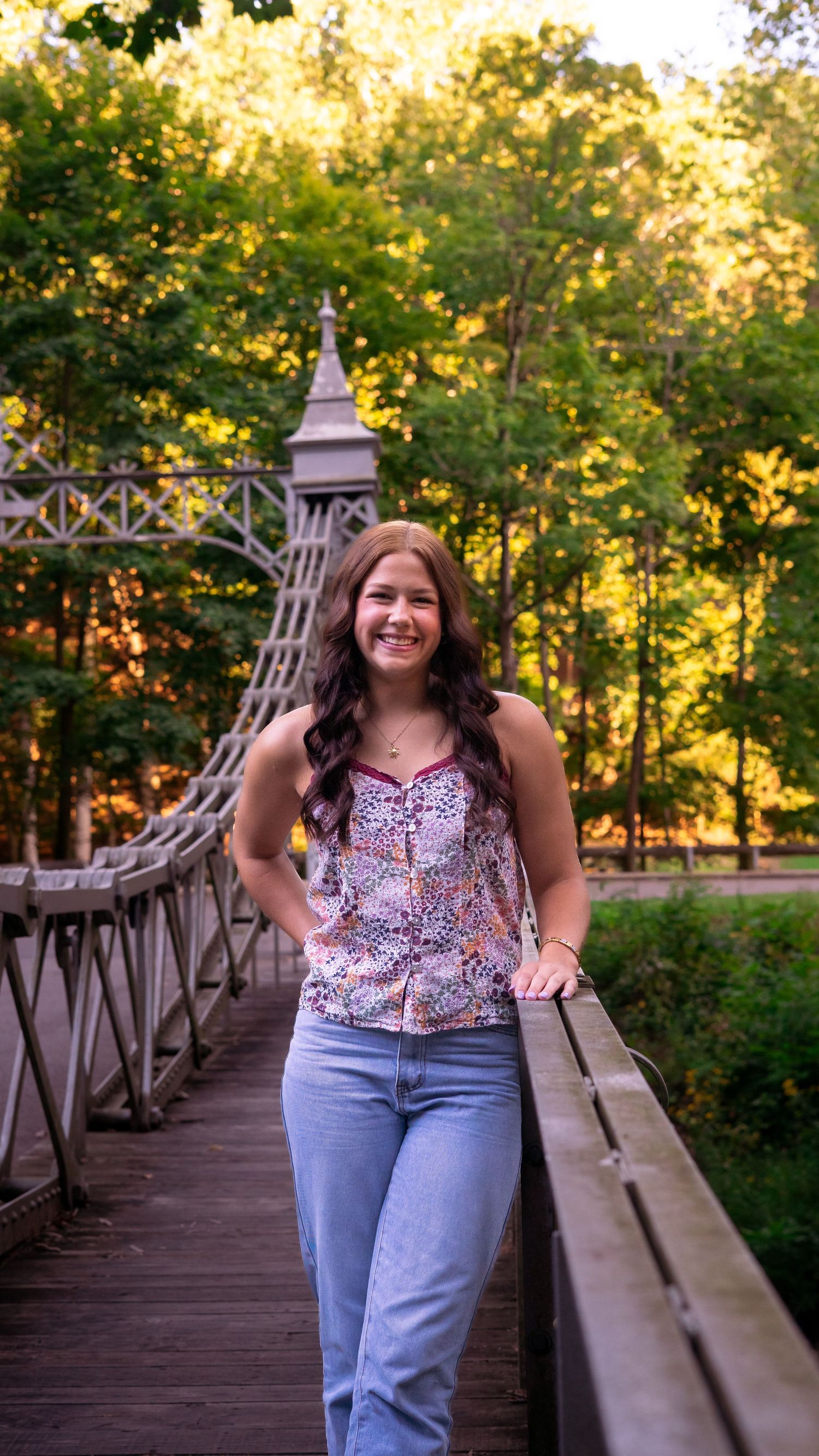 A person in casual attire smiles while standing on a rustic wooden footbridge during golden hour lighting.