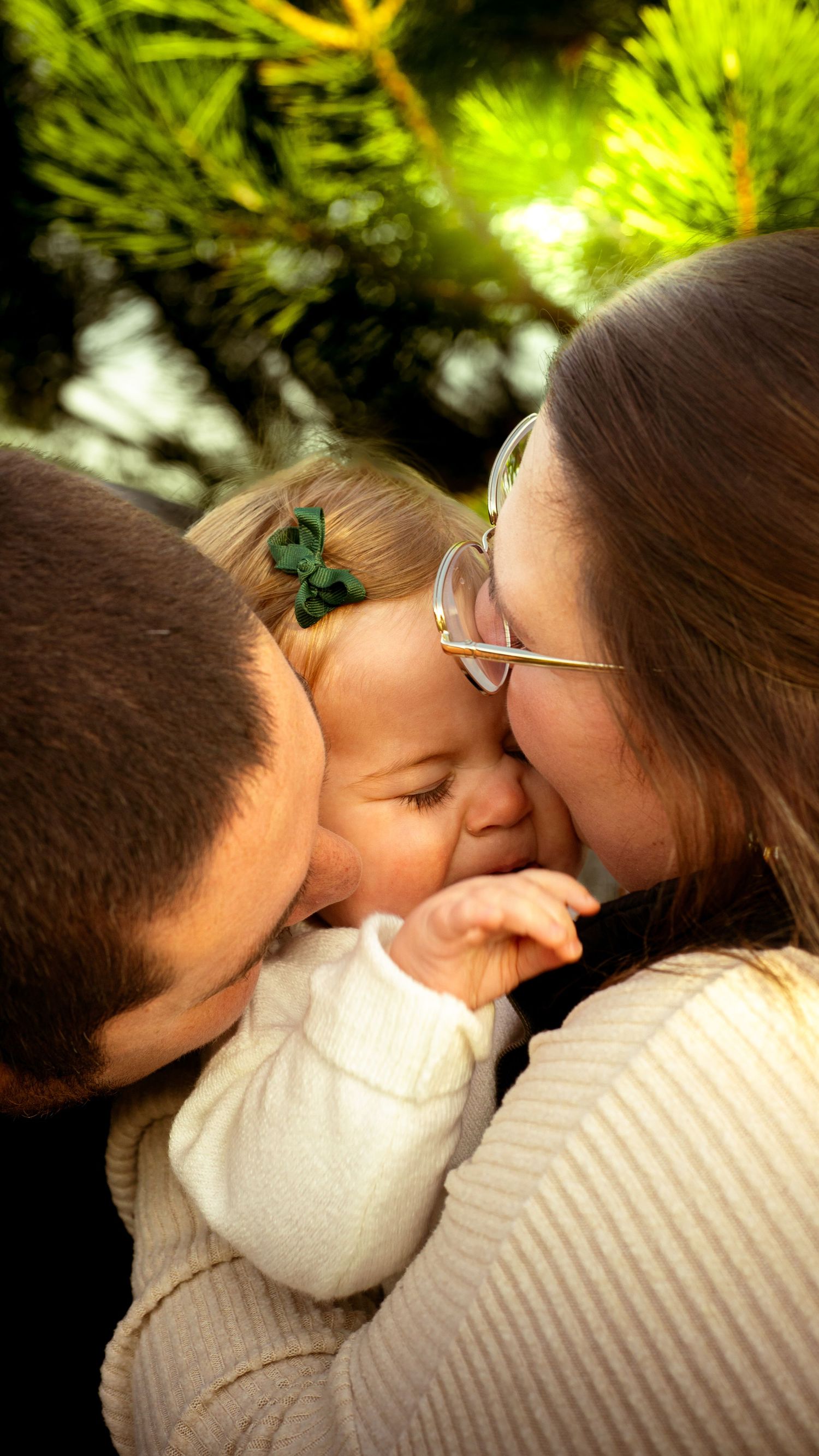 A tender family moment captured outdoors with a small green butterfly clip visible in soft natural lighting.