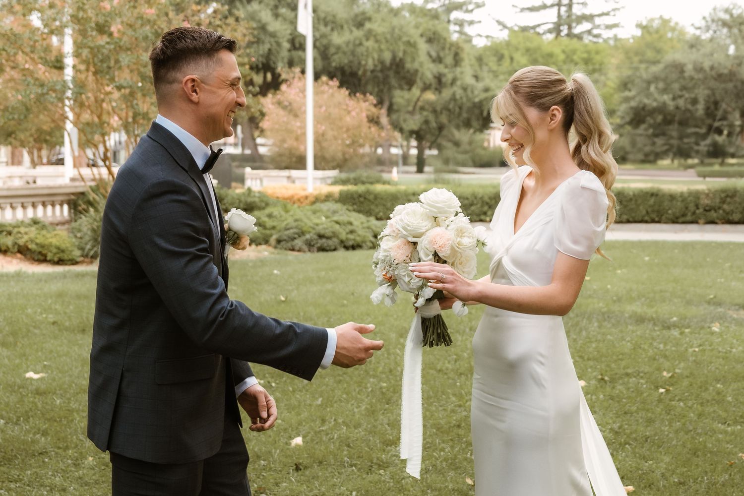 Wedding couple sharing a playful moment outdoors with white floral bouquet.