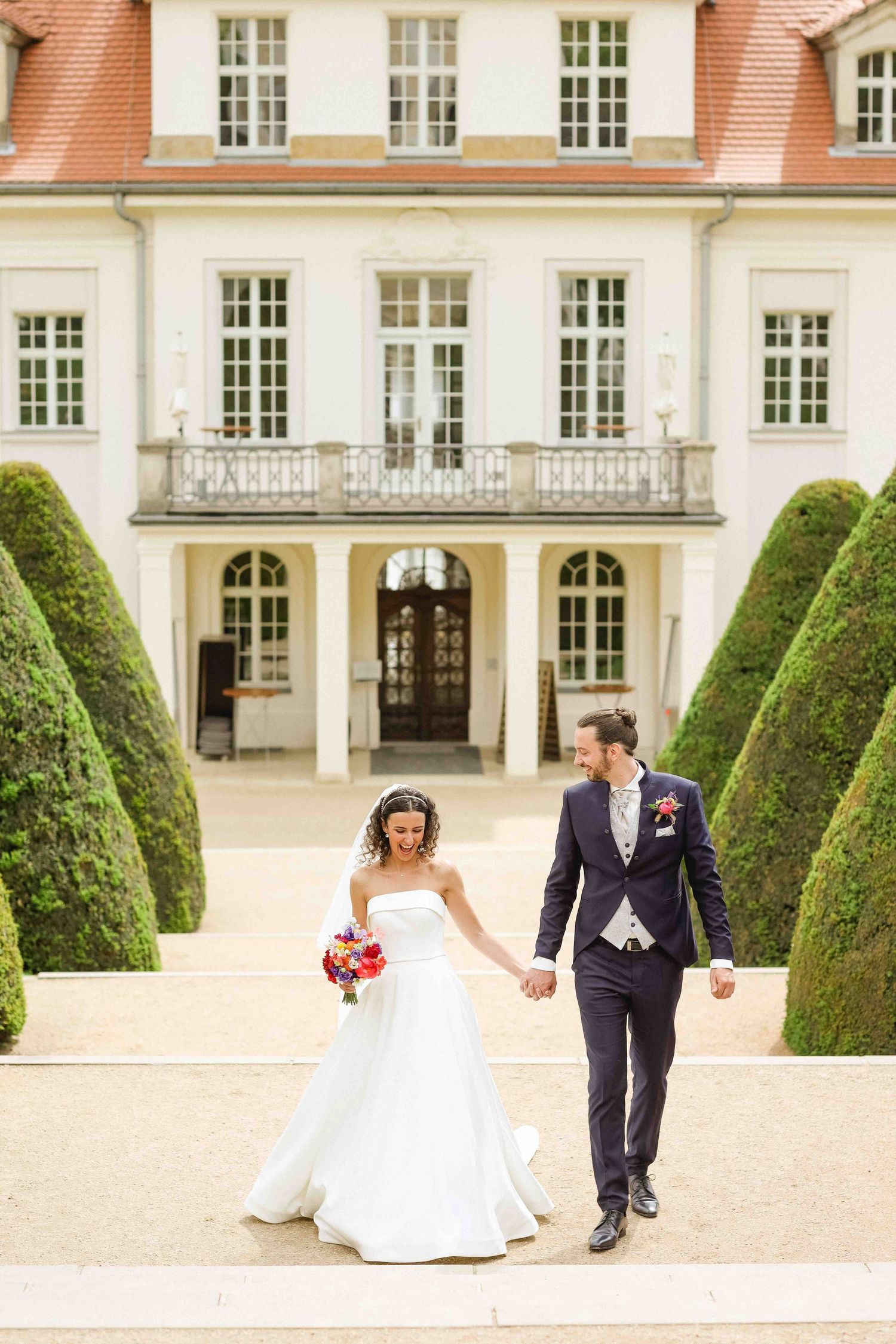 A romantic wedding photo sequence showing the couple walking hand in hand through a garden courtyard of a grand estate.
