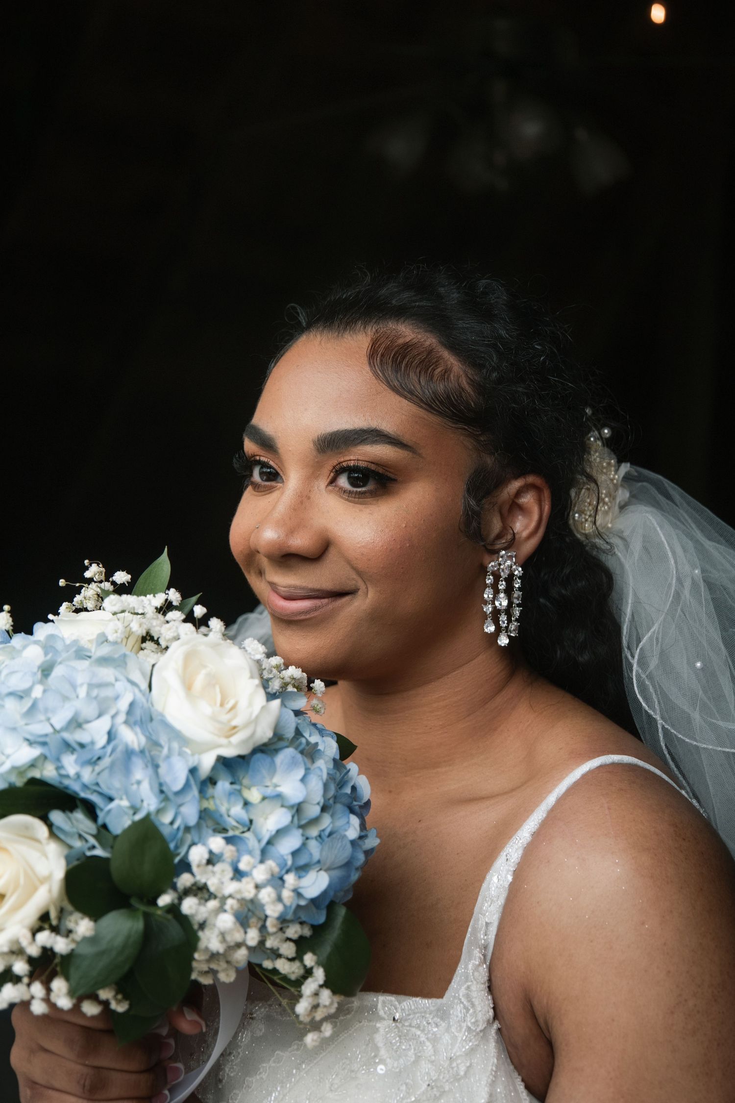 A radiant bride in a white dress holds a stunning bouquet of blue hydrangeas and white roses with a delicate veil.