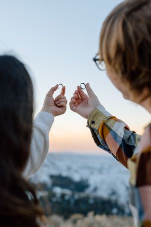 Two people holding rings in front of a sunset cityscape view from above.