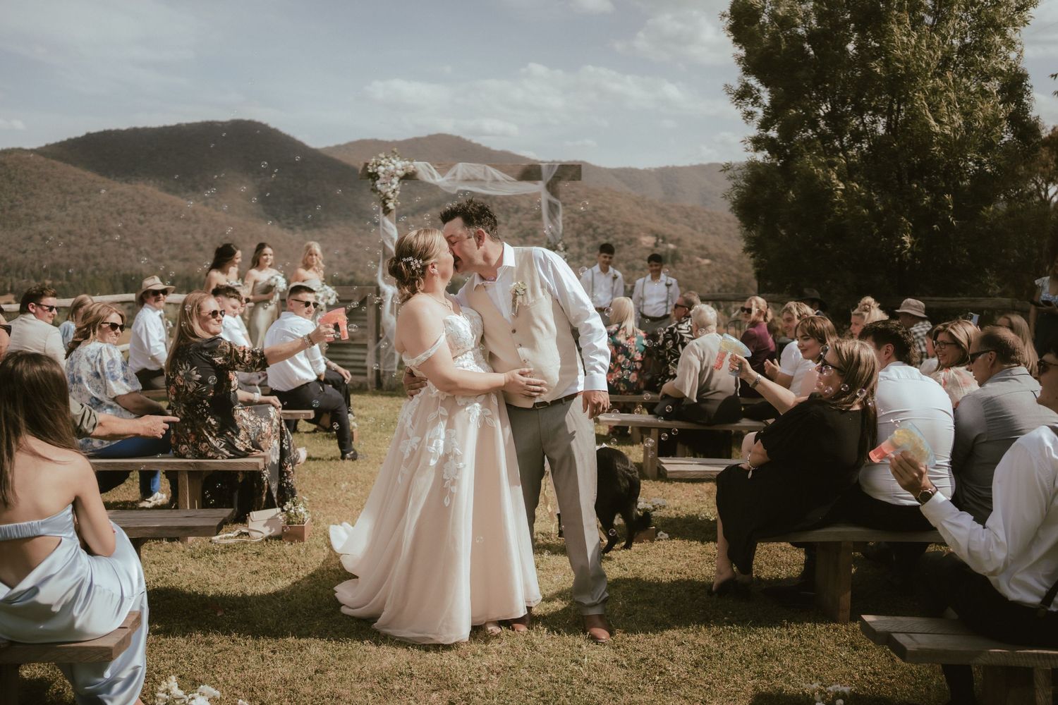 Wedding guests enjoy outdoor celebration in rustic mountain setting during golden hour against rolling hills backdrop at Howqua Lodge