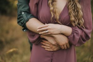 A close-up of couples hands and an engagement ring in a soft outdoor setting against a blurred natural background.