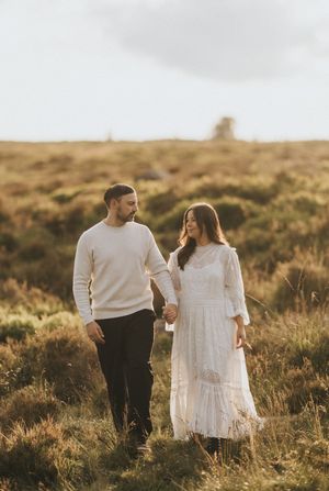 Couple walking together through golden grass field at sunset holding hands in engagement photo session. Taken by Lincolnshire photographers.