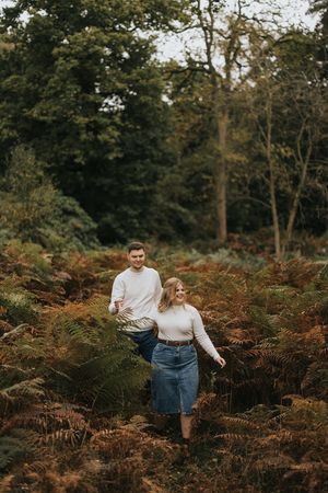 Two people walking through autumn ferns and trees in a moody woodland setting during engagement shoot captured by Lincolnshire photographers