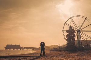 Two silhouettes embrace against a beautiful sunset with Cleethorpes ferris wheel creating a romantic carnival scene.