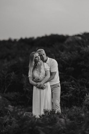 A romantic black and white photo showing a couple embracing against a dark natural outdoor background.