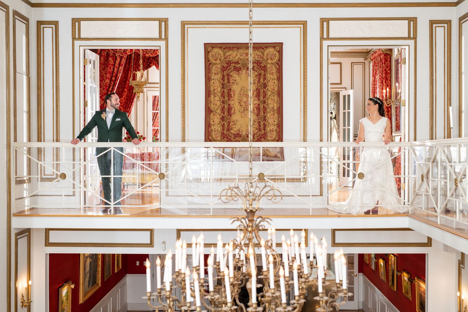 Ornate white and gold paneled ballroom with crystal chandeliers and red drapery in an elegant palace interior.