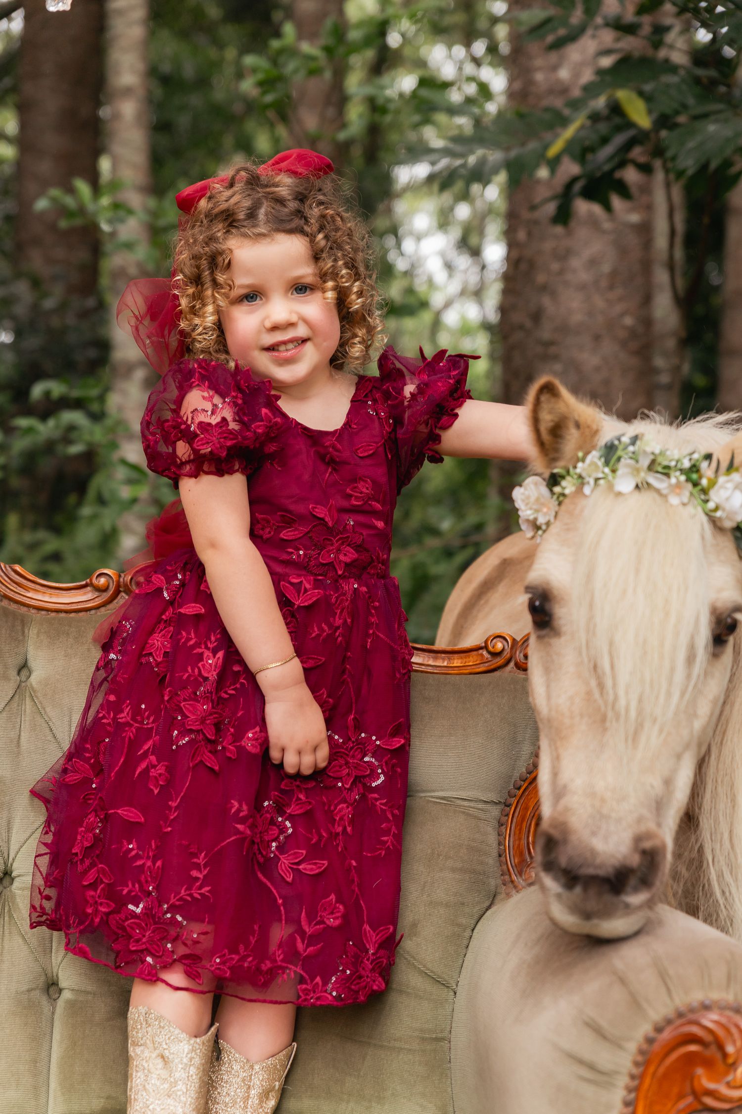 Red dress photoshoot featuring a vintage sofa and decorated horse in a woodland setting.