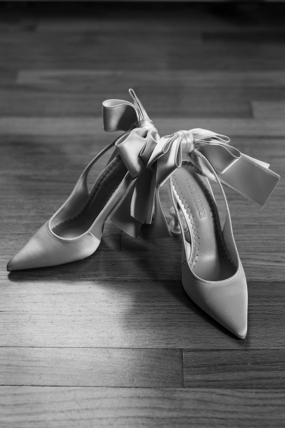 Elegant white pointed-toe bridal shoes arranged on hardwood floor.
