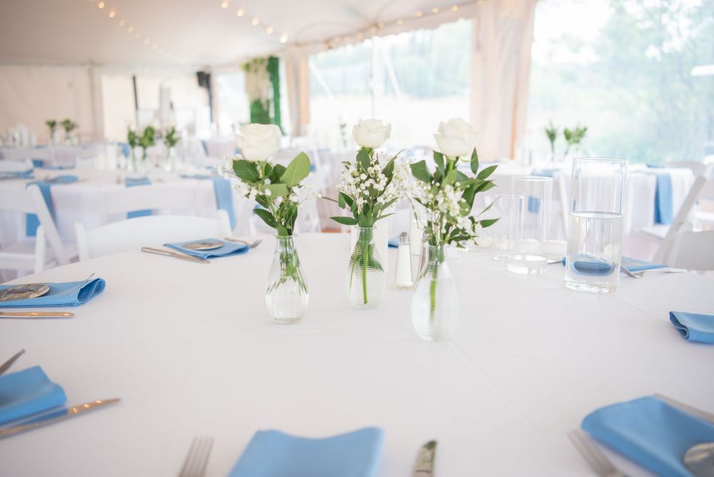 White wedding reception tent with blue accents and floral centerpieces.