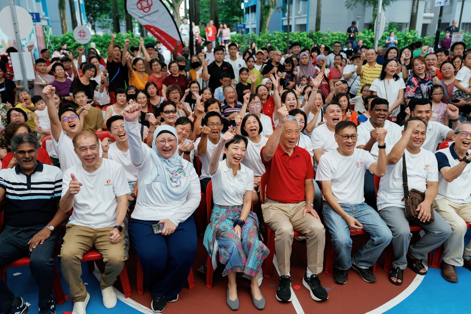 Large crowd of people in white and casual attire sitting together for an outdoor event or gathering.