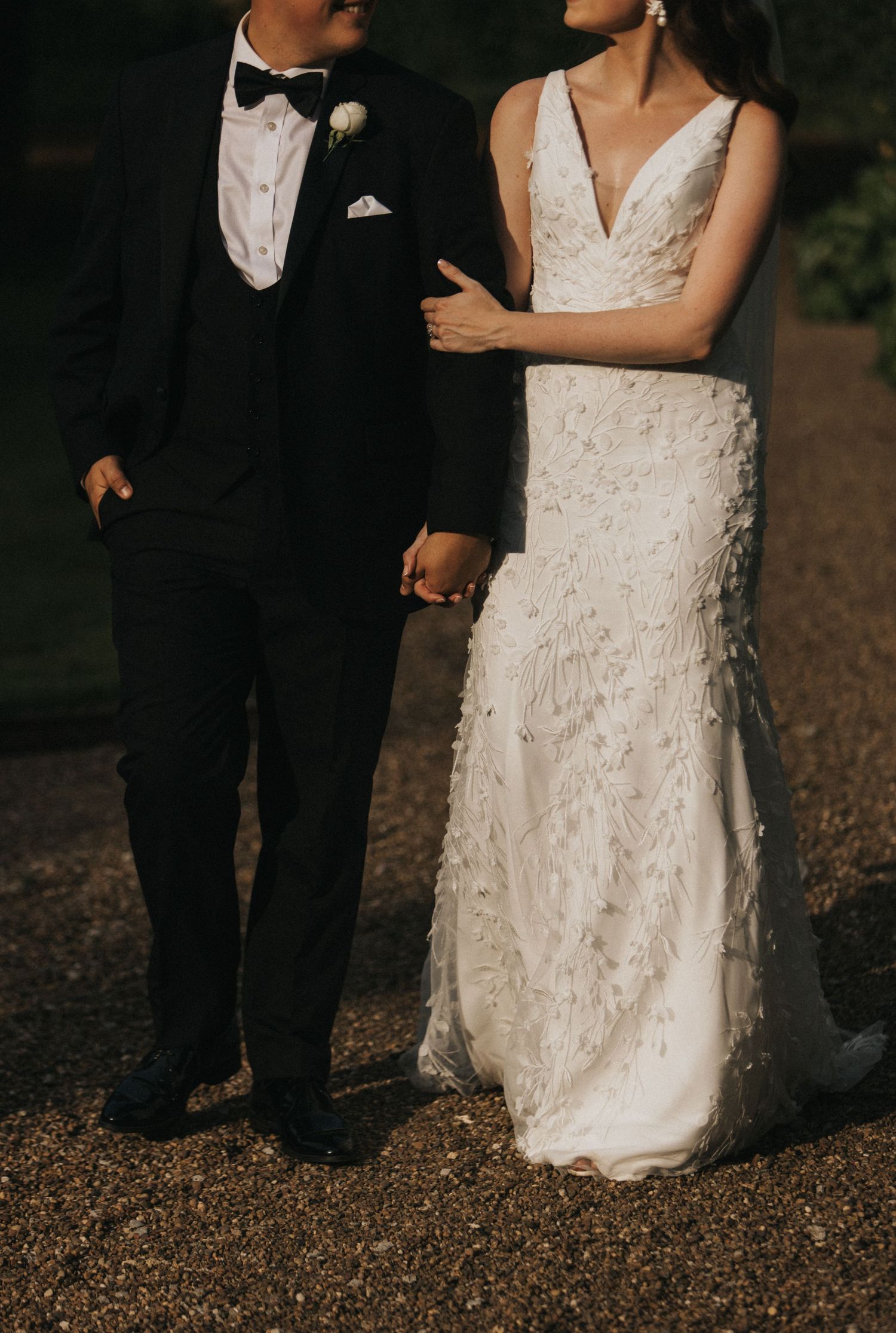 Close-up details of lace wedding dress and black tuxedo during an outdoor forest wedding ceremony.