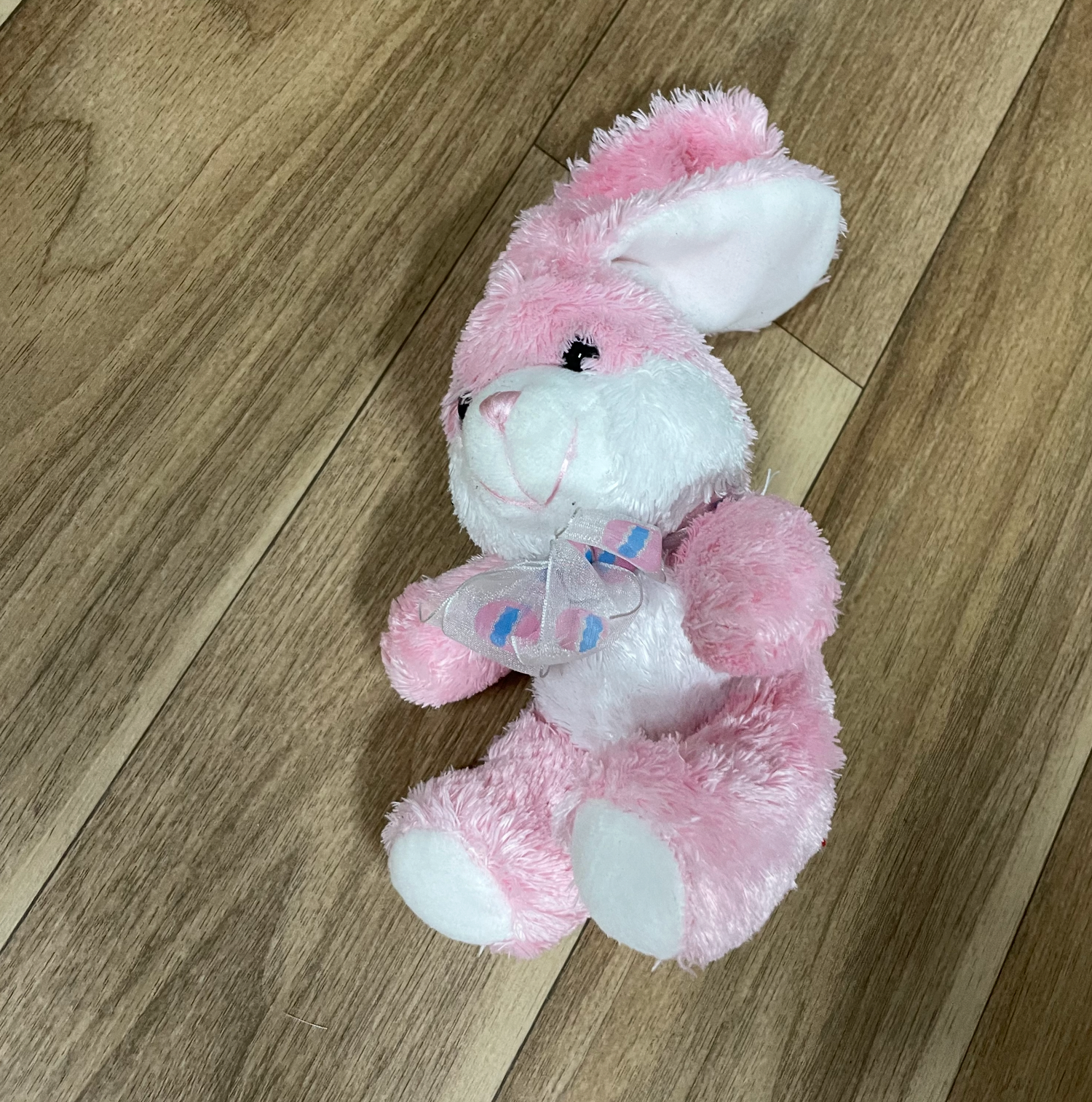 Pink and white plush bunny toys displayed on hardwood flooring.