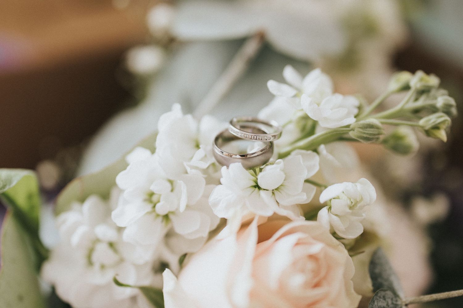 Wedding rings sit on elegant blush pink roses and white hydrangeas arranged in a romantic wedding bouquet.