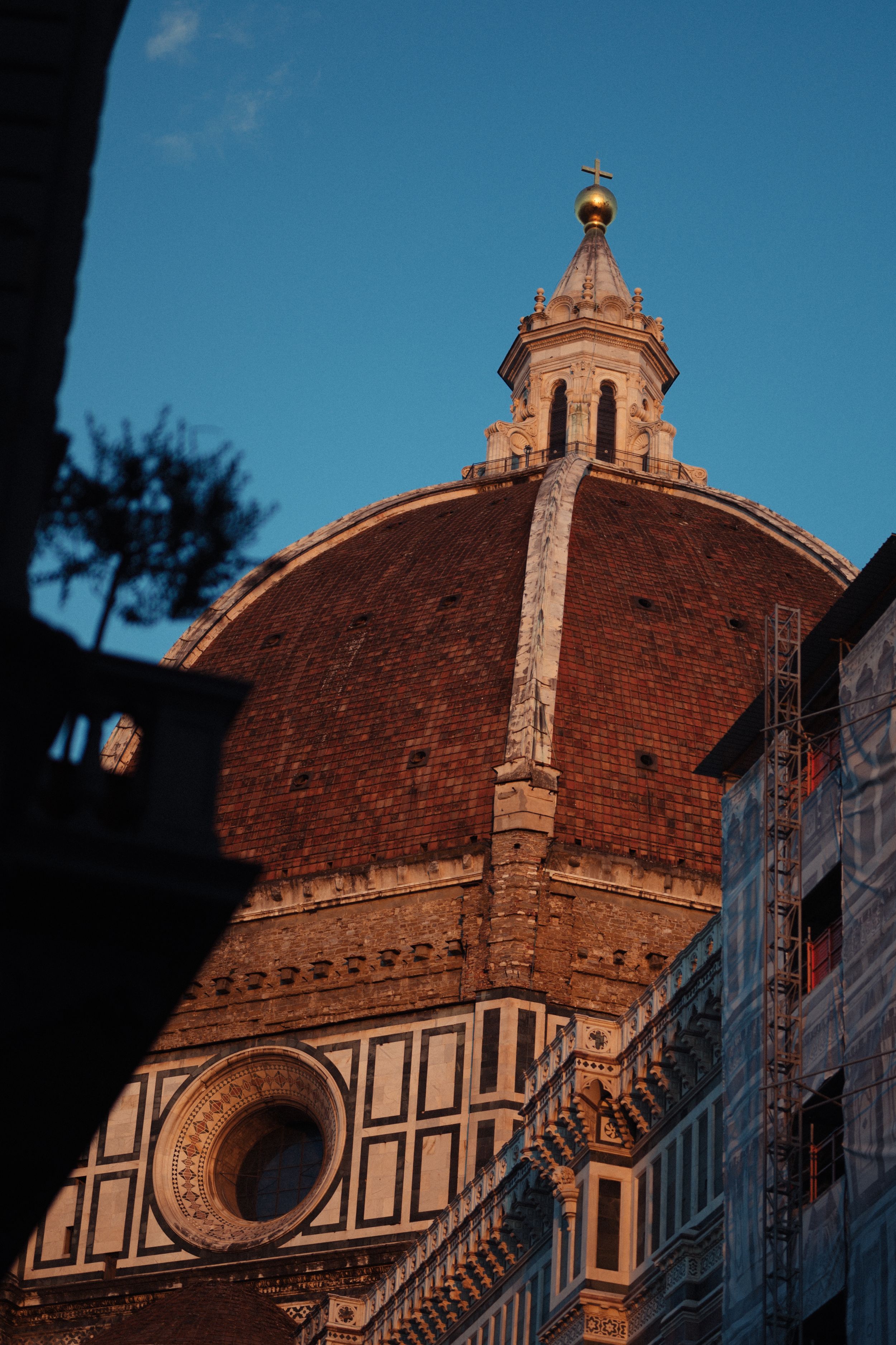 The iconic dome of Florence's Duomo cathedral catches golden sunlight during sunset against a deep blue sky.