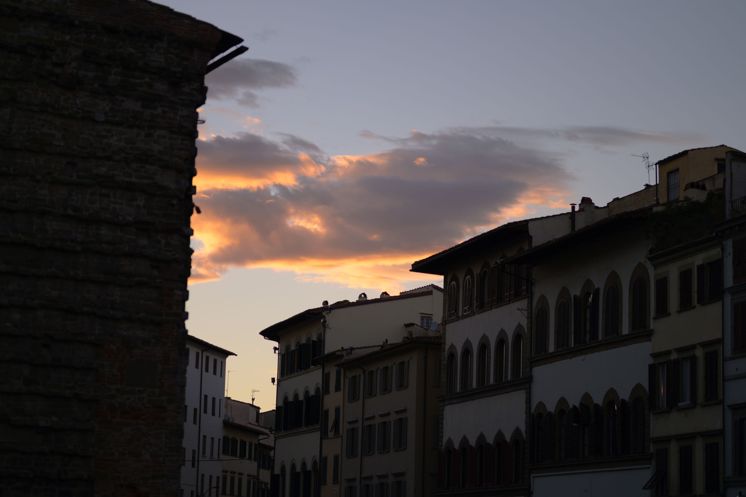 Historic buildings silhouetted against a dramatic sunset sky with orange clouds in Florence, Italy.