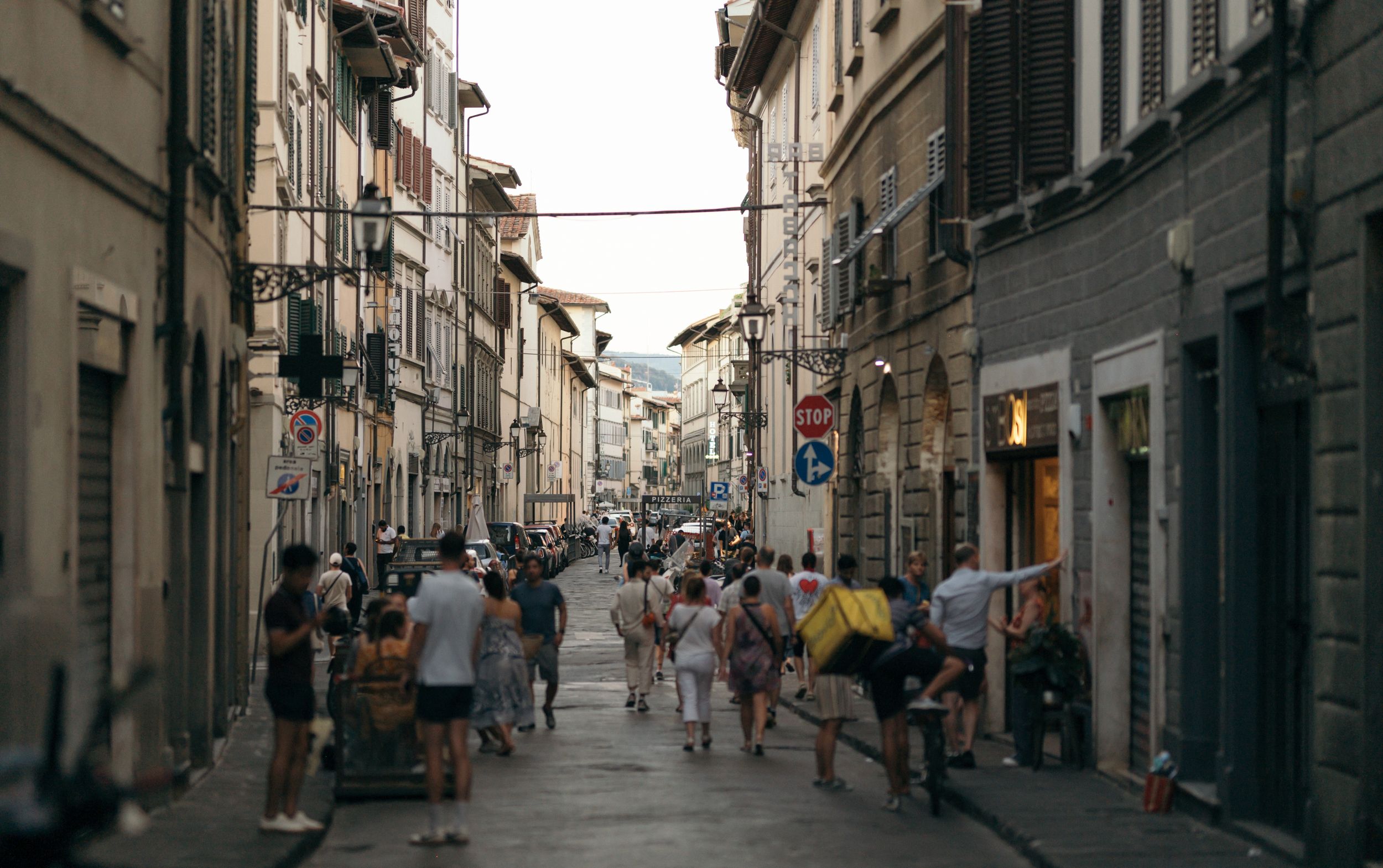 Busy pedestrian street in an old European city with historic buildings and storefronts on a summer day.