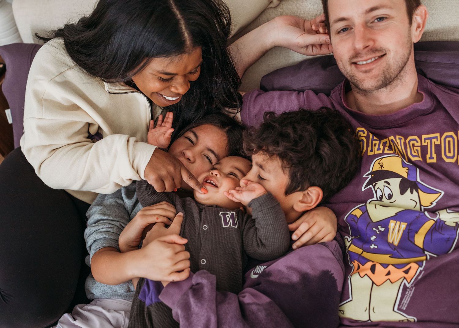 A heartwarming scene of family members laughing and cuddling together on a bed with purple bedding.