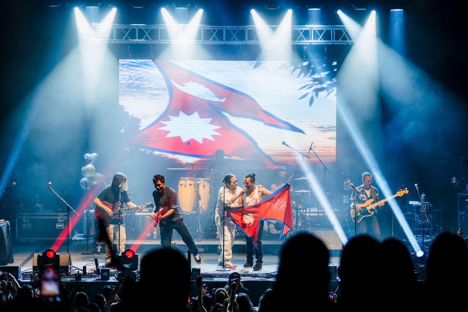 Rock band performs on stage with bright blue spotlights and dramatic backdrop displaying shark imagery during concert.