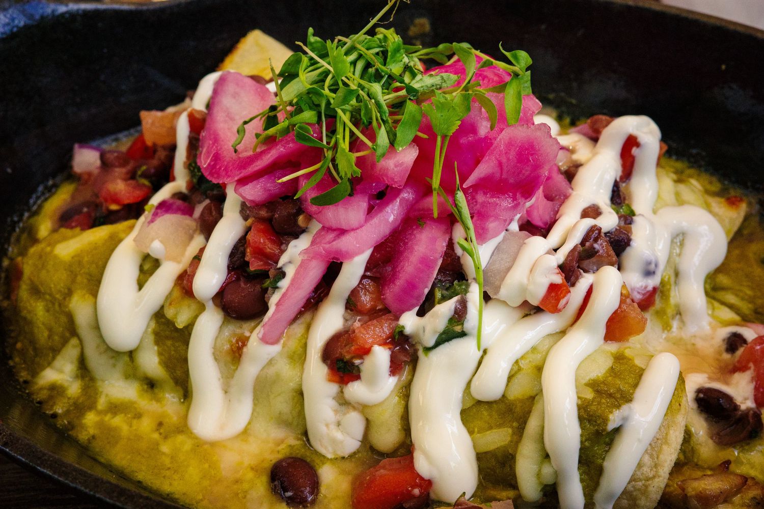 Mexican enchiladas topped with green sauce, black beans, pickled red onions, and sour cream drizzle.