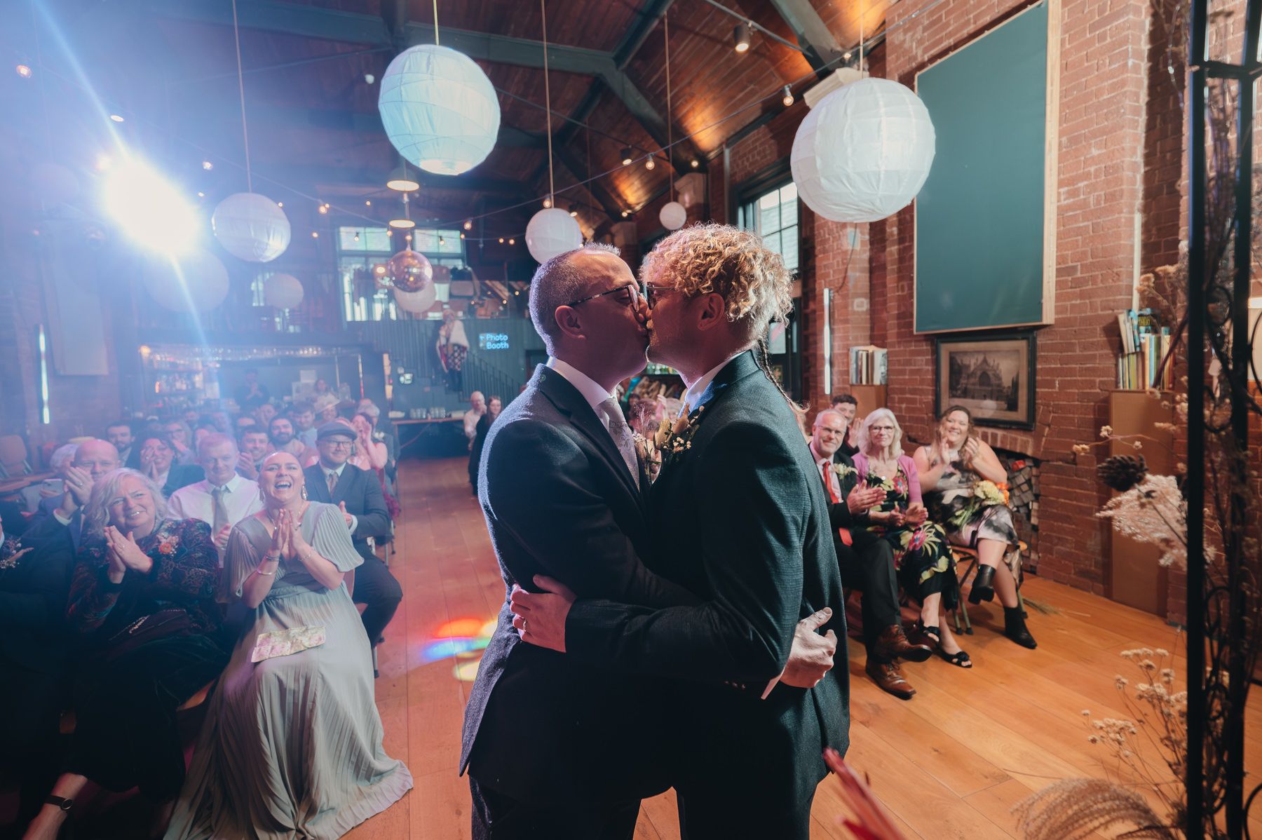 A couple shares their first dance at a wedding reception with hanging paper lanterns and guests watching from tables.