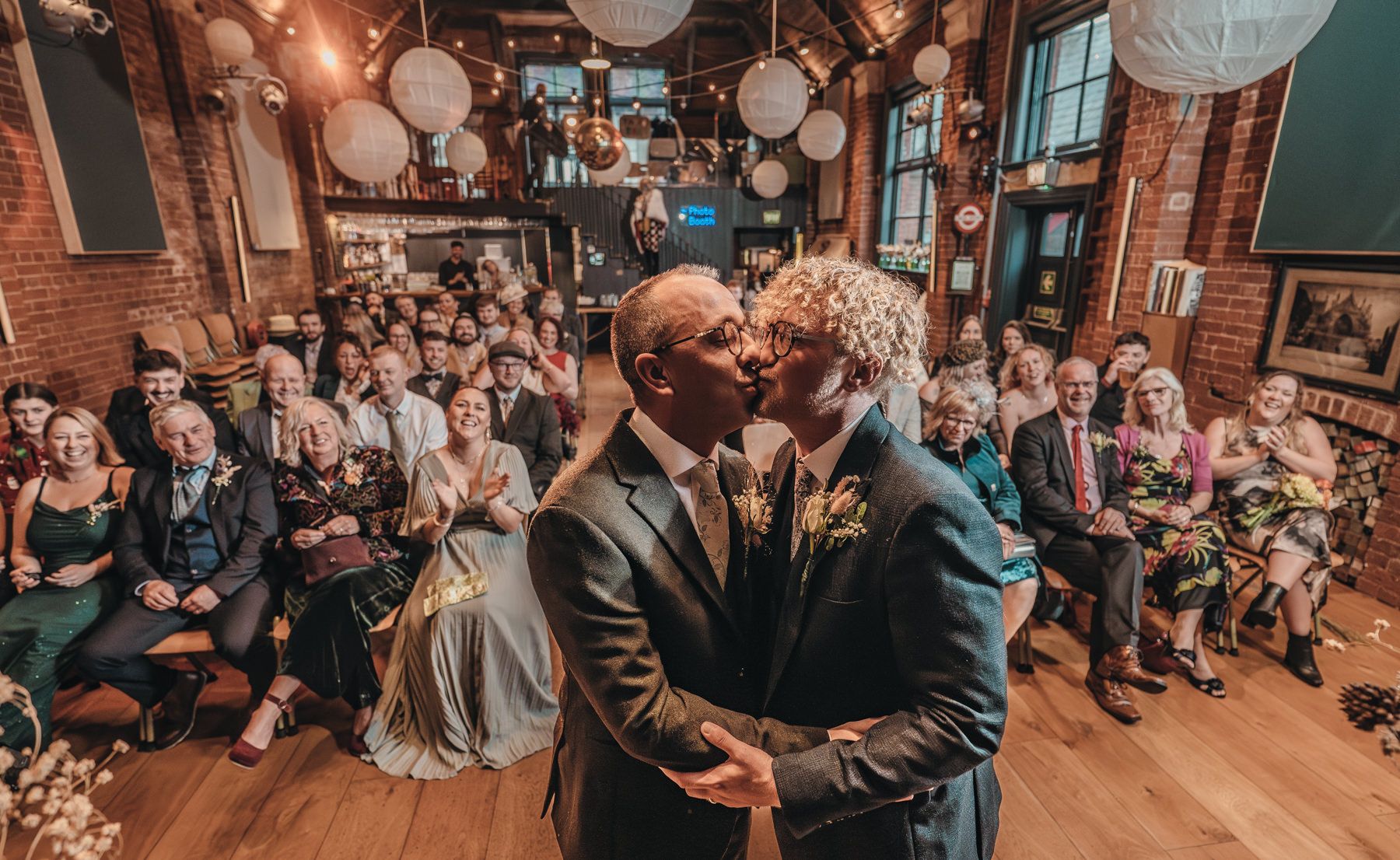 Large rustic venue with exposed brick walls and white paper lanterns hosting a formal social gathering event.