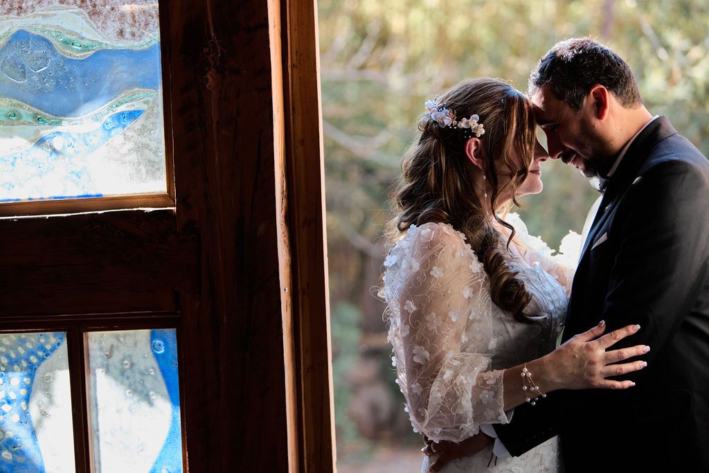Intimate romantic wedding scene near window showing couple embracing in a rustic cabin setting.
