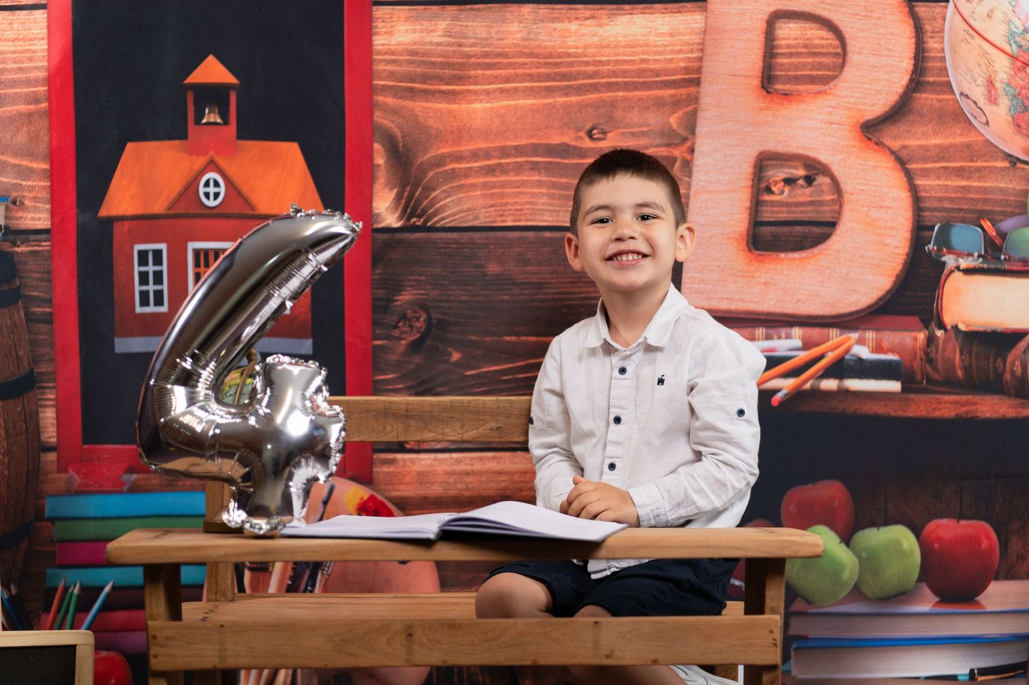 Student in white shirt sitting at wooden desk with school supplies and decorative background.