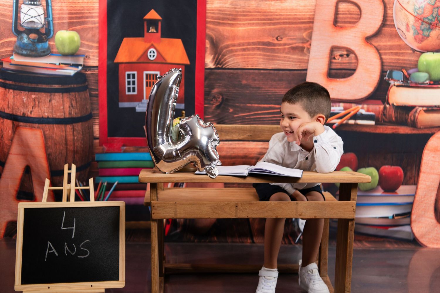 Classroom setting with wooden desk and red schoolhouse decorations on wall.