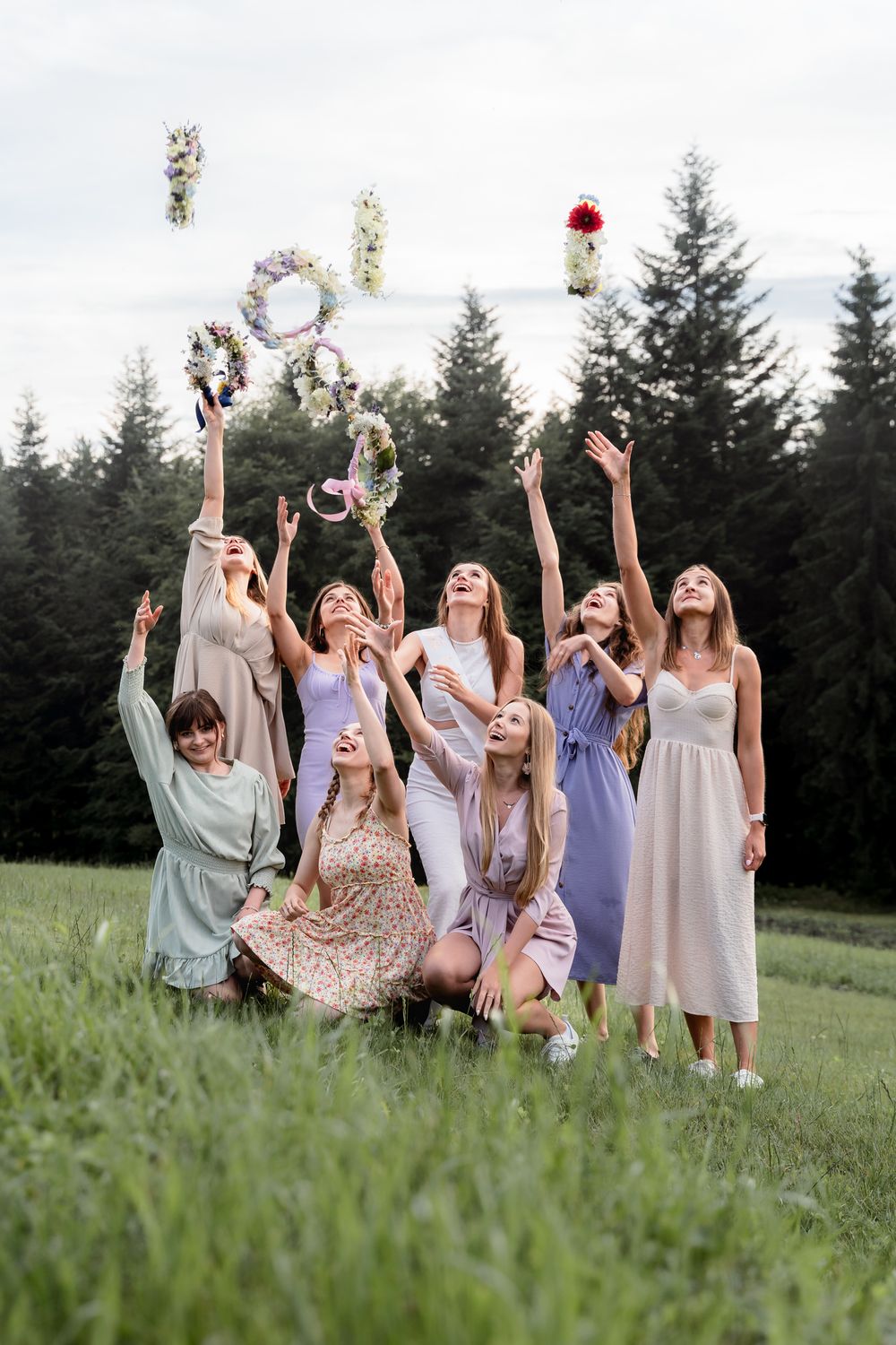 Przyjaciółki bawią się podczas sesji wieczoru panieńskiego w Beskidach, podrzucają wianki w boho stylu, spontaniczne zdjęcia w lesie