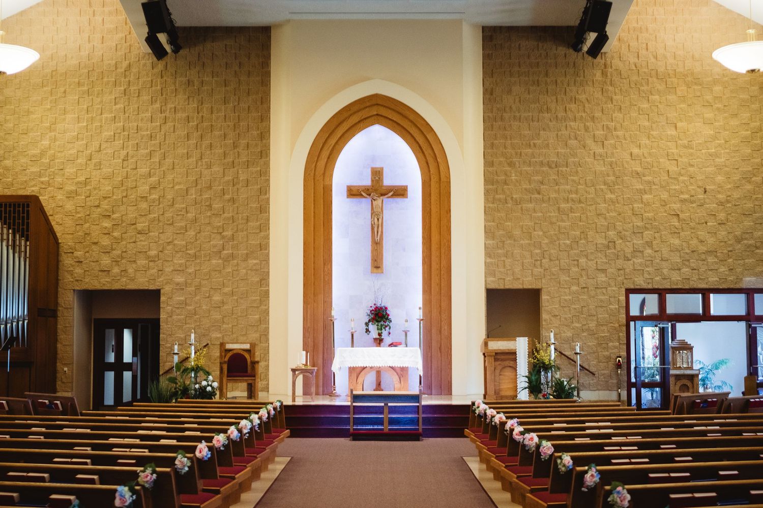 Interior view of a church sanctuary with wooden pews, golden walls, and a large cross mounted in an arched altar area.