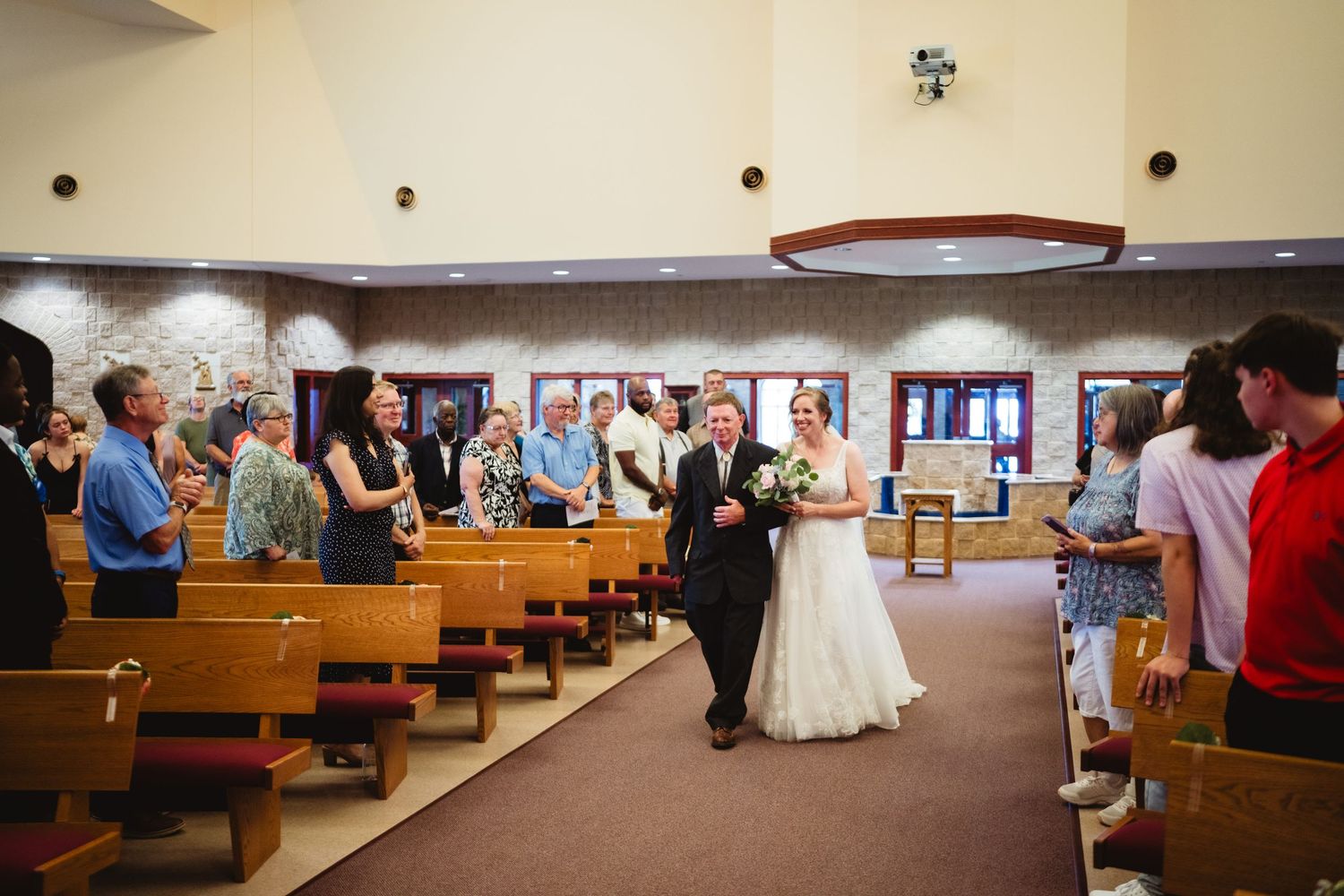 Wedding reception dinner guests seated at long wooden pews in a church reception hall.