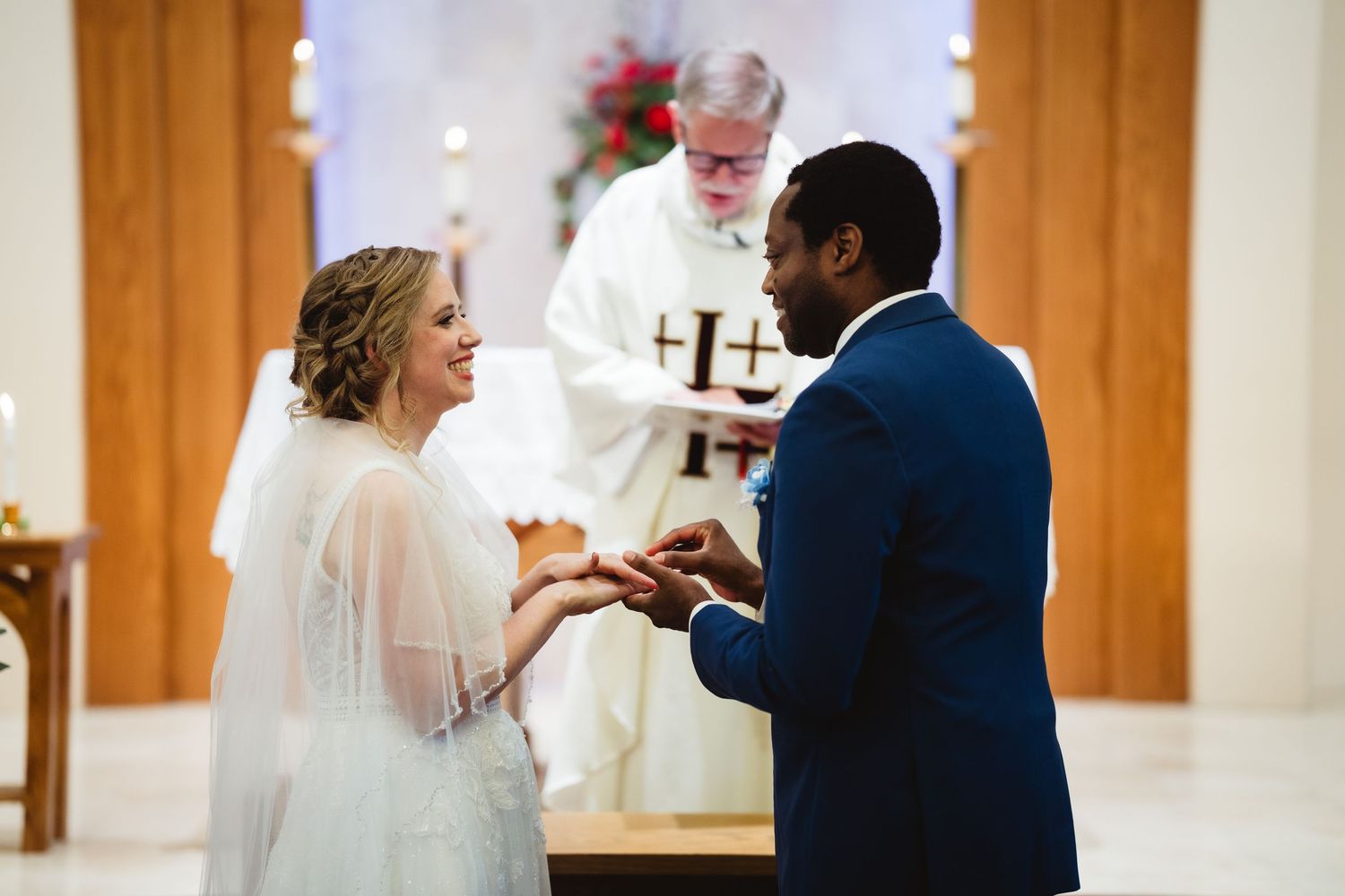 A bride and groom exchange rings during their wedding ceremony as an officiant stands behind them at the altar.