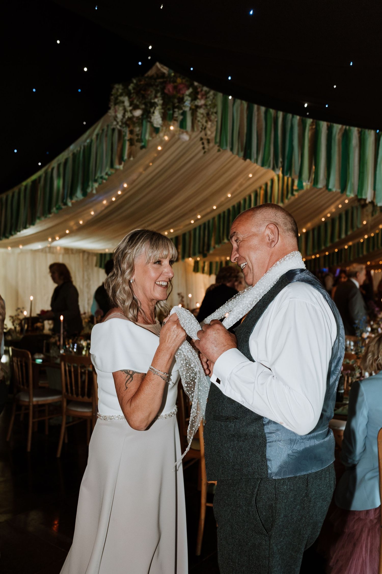 Dancing couple shares a tender moment together on a wedding dance floor under twinkling string lights and green decor.