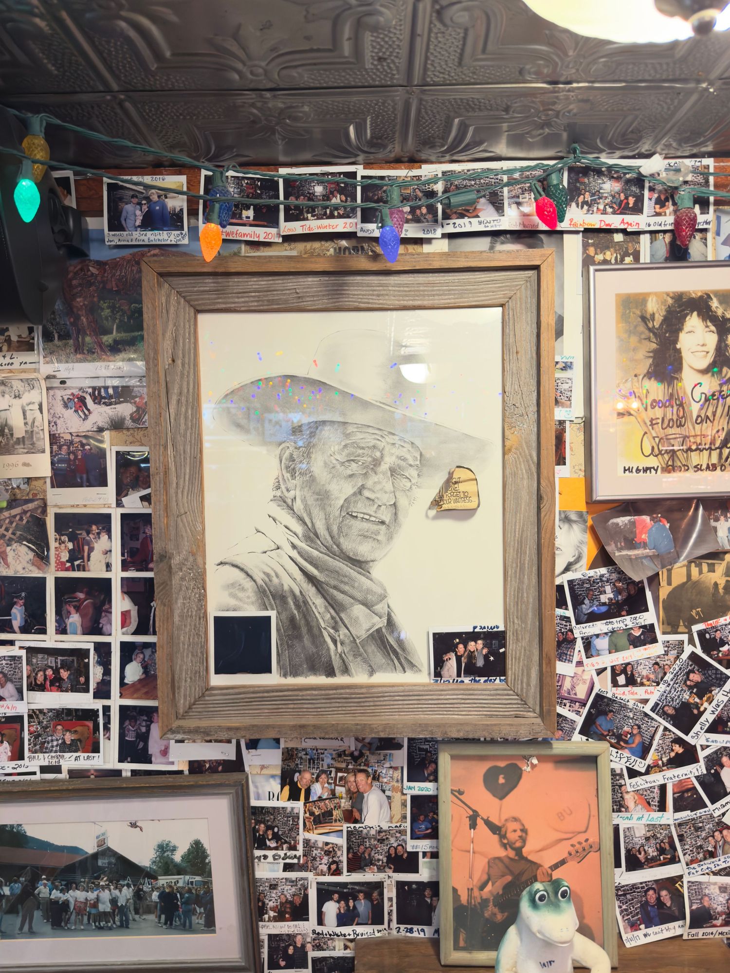 Framed pencil sketch of a cowboy surrounded by photos and memorabilia on a wall.