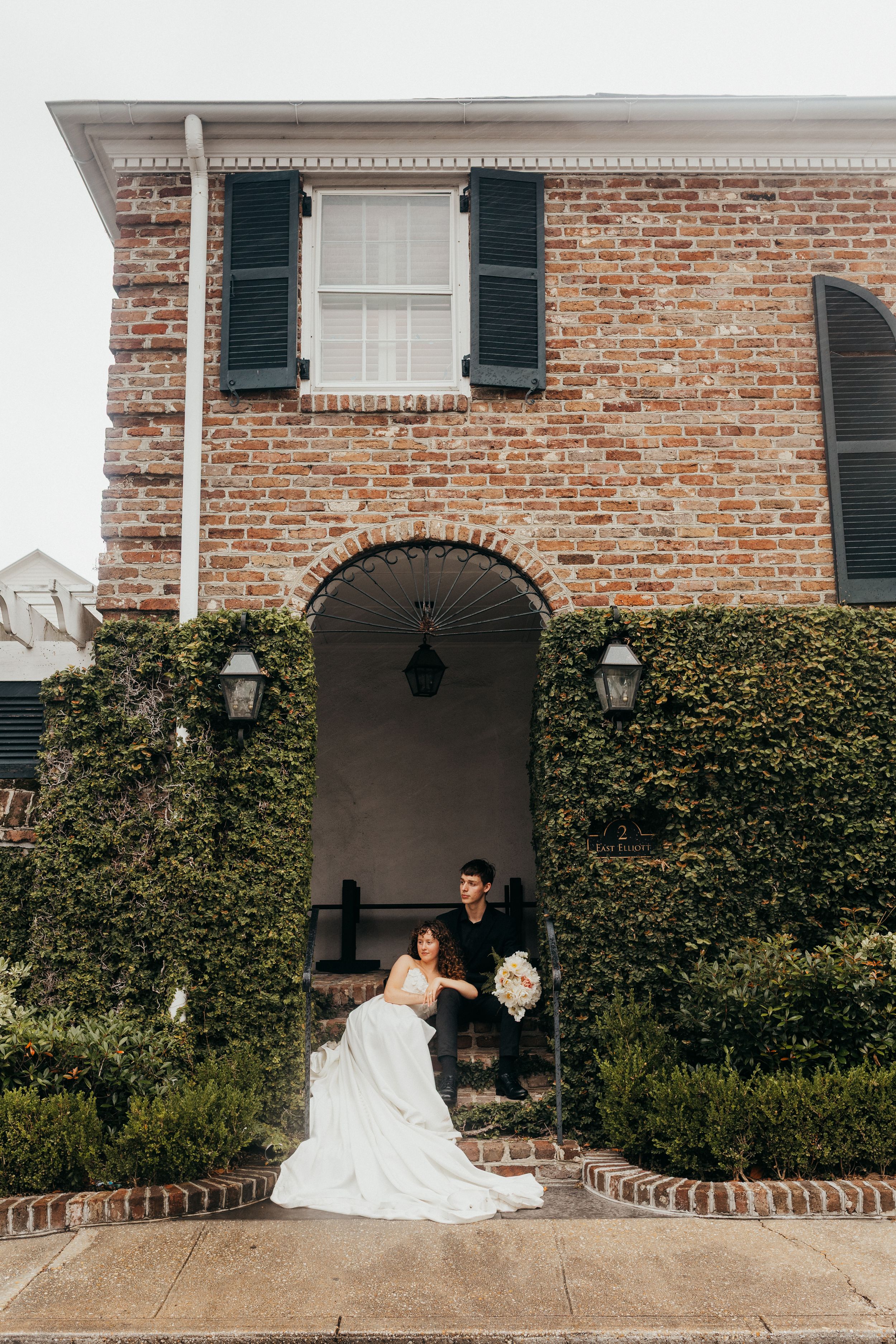 Elegant brick building entrance with arched doorway and climbing ivy features black shutters and traditional lanterns.