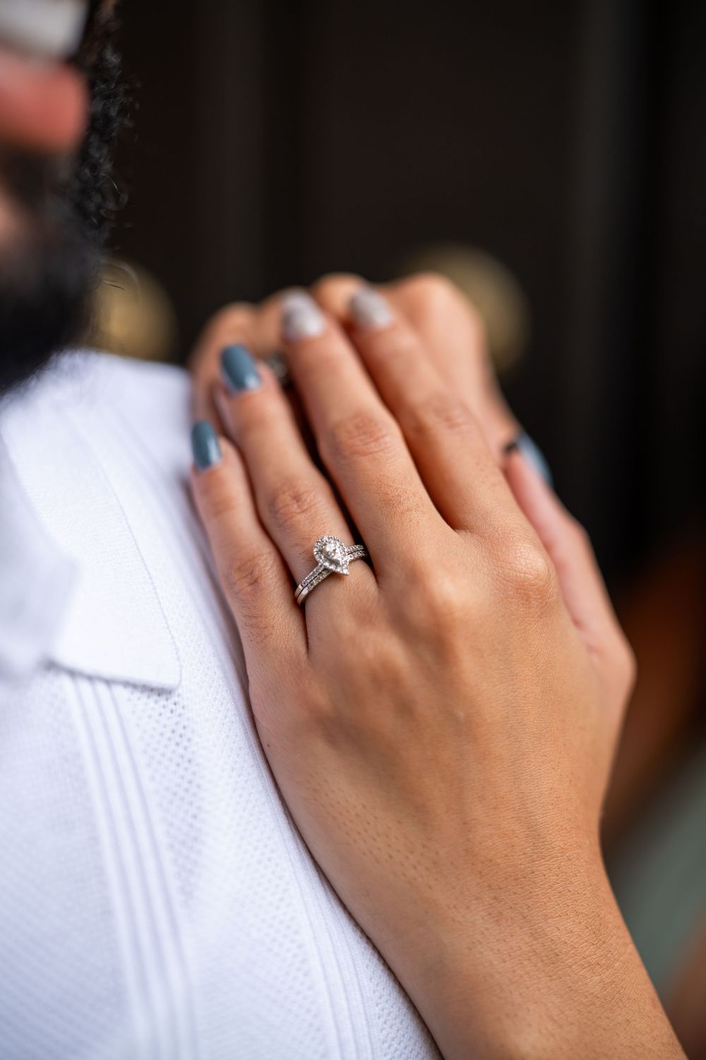 Close-up of a hand with blue painted nails and diamond engagement ring resting on white fabric.