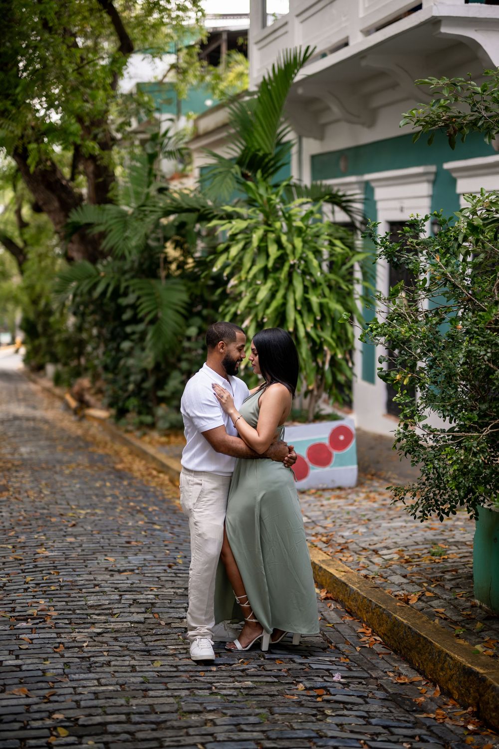 Two people share an intimate moment while sitting on wooden benches along a cobblestone path surrounded by lush greenery.